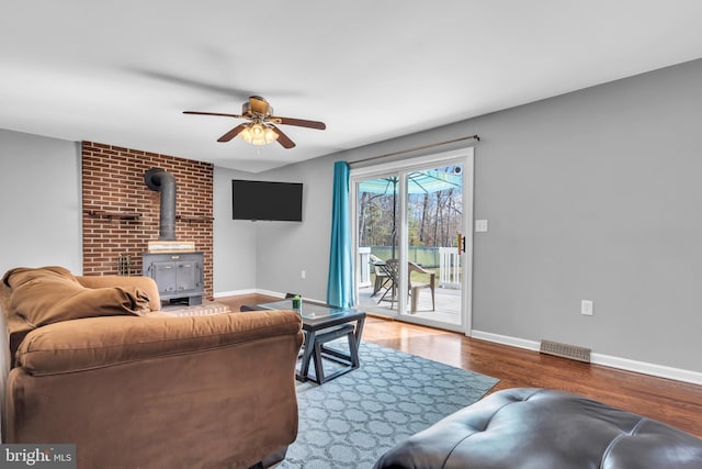living area with a wood stove, baseboards, visible vents, ceiling fan, and wood finished floors