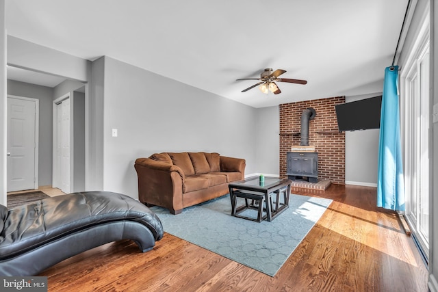 living area with wood finished floors, a wood stove, and a ceiling fan