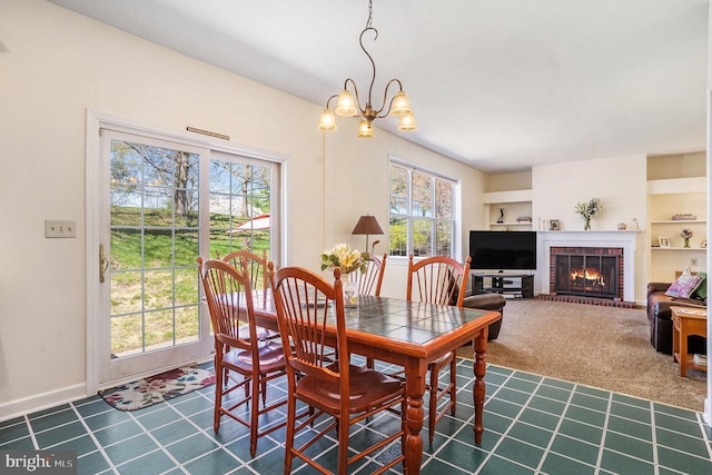 dining room with baseboards, built in shelves, dark colored carpet, an inviting chandelier, and a fireplace