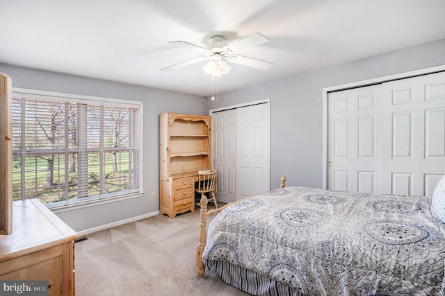 bedroom featuring light carpet, baseboards, two closets, and a ceiling fan