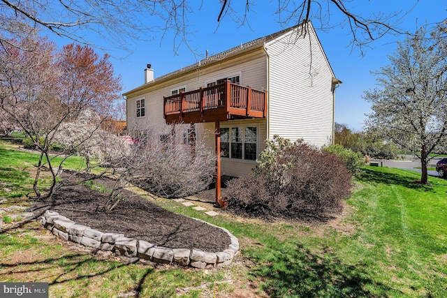 back of property with a wooden deck, a lawn, and a chimney