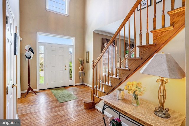 foyer with wood-type flooring, baseboards, stairway, and a high ceiling
