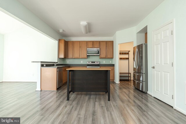 kitchen featuring stainless steel appliances, wood finished floors, a kitchen island, and brown cabinetry