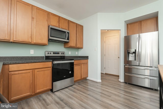 kitchen featuring dark countertops, brown cabinets, light wood-style flooring, baseboards, and appliances with stainless steel finishes