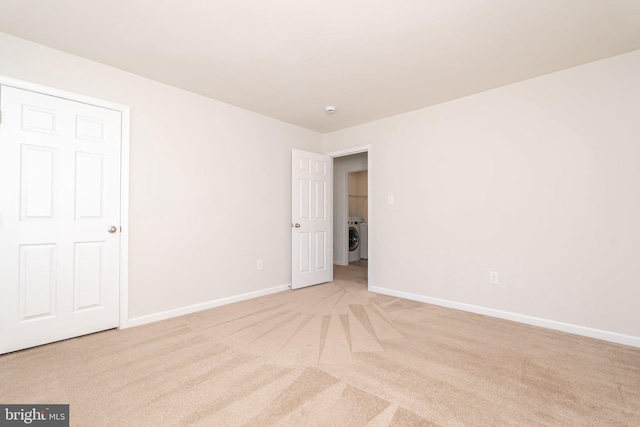 unfurnished bedroom featuring light carpet, washer / dryer, and baseboards