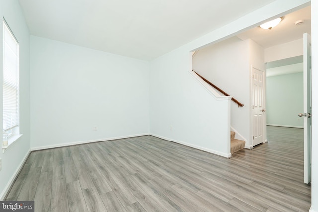 unfurnished living room with light wood finished floors, baseboards, and stairway
