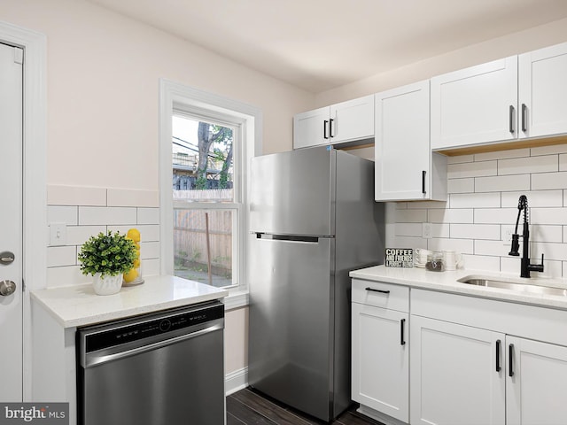 kitchen featuring backsplash, light stone countertops, a sink, stainless steel appliances, and white cabinetry