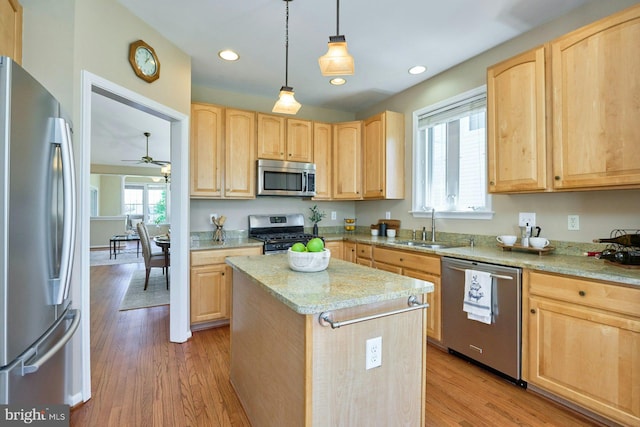 kitchen with a sink, appliances with stainless steel finishes, light brown cabinets, and a center island