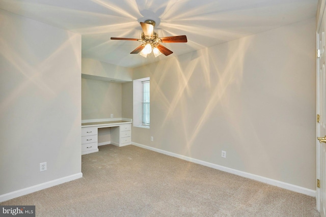 unfurnished bedroom featuring built in study area, baseboards, ceiling fan, and light colored carpet