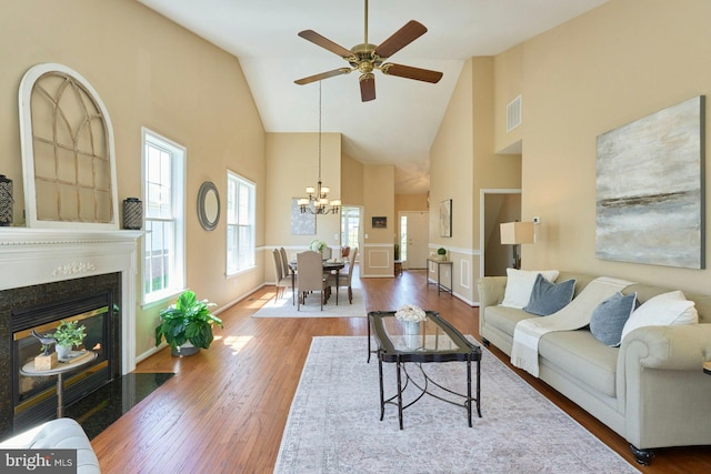 living room featuring visible vents, a fireplace with flush hearth, wood finished floors, high vaulted ceiling, and ceiling fan with notable chandelier