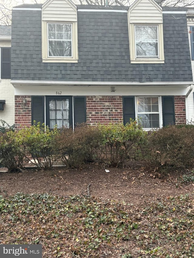 view of front of house featuring brick siding, roof with shingles, and a gambrel roof