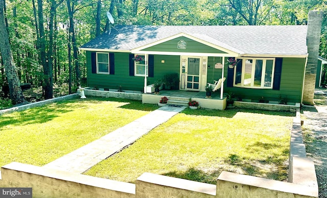 view of front of home with a porch, a front yard, a shingled roof, and a chimney
