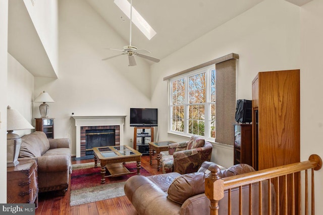 living room with ceiling fan, a fireplace, high vaulted ceiling, a skylight, and wood finished floors