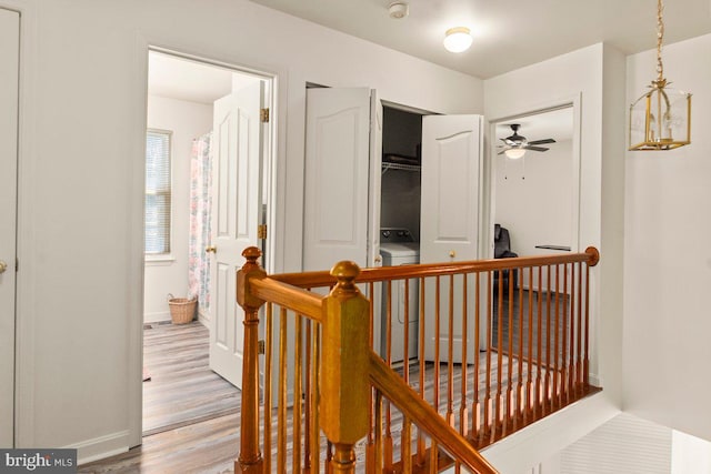 corridor featuring washer / clothes dryer, wood finished floors, baseboards, and an upstairs landing