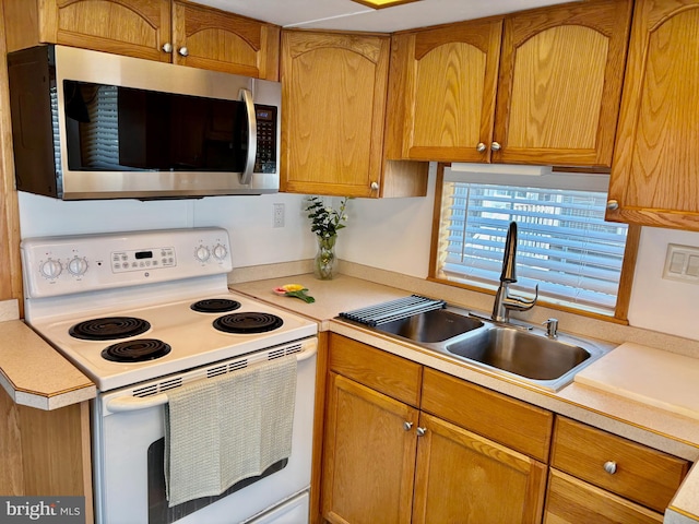 kitchen featuring white electric range oven, a sink, brown cabinets, light countertops, and stainless steel microwave