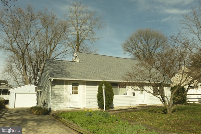 new england style home featuring a garage, an outdoor structure, roof with shingles, and concrete driveway