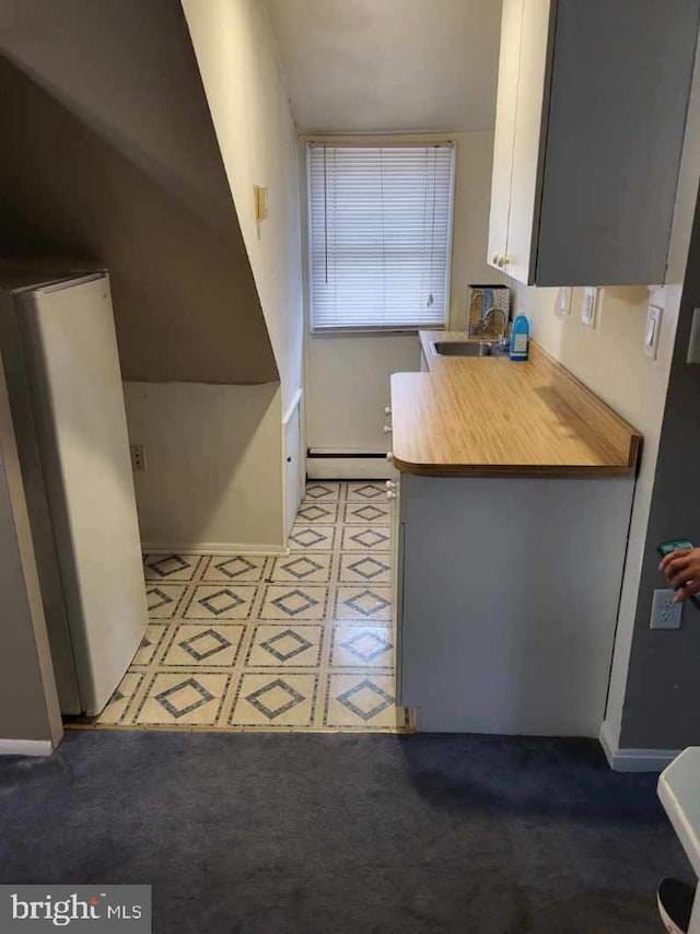 kitchen with tile patterned floors, a sink, baseboards, a baseboard radiator, and white cabinetry