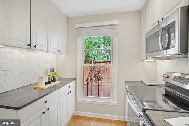kitchen with stainless steel appliances, white cabinets, backsplash, light wood-style floors, and baseboards