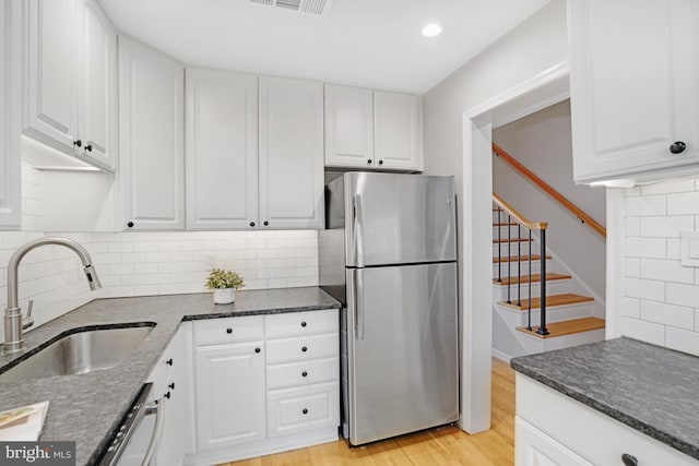 kitchen with freestanding refrigerator, a sink, dishwasher, light wood-style flooring, and white cabinetry