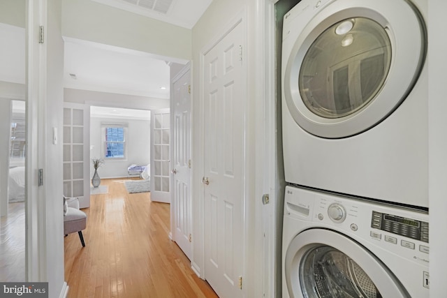 clothes washing area featuring estacked washer and dryer, light wood-style flooring, and baseboards