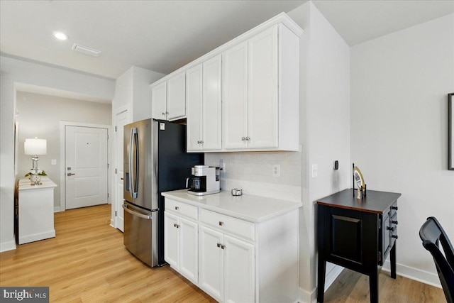 kitchen featuring light wood finished floors, stainless steel refrigerator with ice dispenser, baseboards, and white cabinetry
