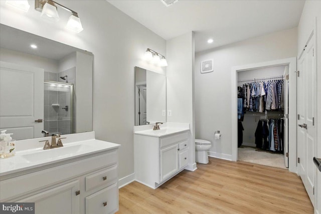 bathroom with recessed lighting, a shower stall, wood finished floors, a sink, and two vanities
