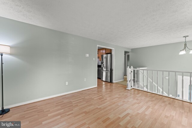 spare room with a textured ceiling, a notable chandelier, baseboards, and light wood finished floors