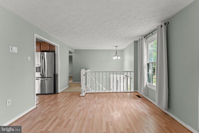 empty room featuring a textured ceiling, visible vents, and light wood finished floors