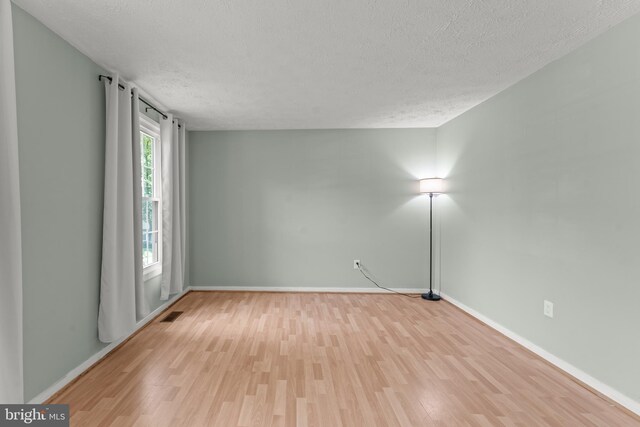 empty room featuring baseboards, a textured ceiling, and light wood finished floors