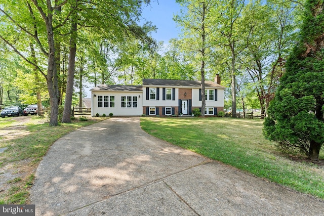raised ranch with concrete driveway, fence, a chimney, and a front yard