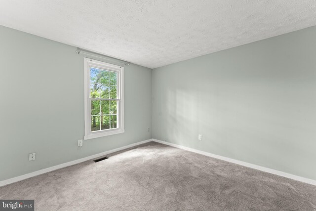 carpeted spare room featuring visible vents, a textured ceiling, and baseboards