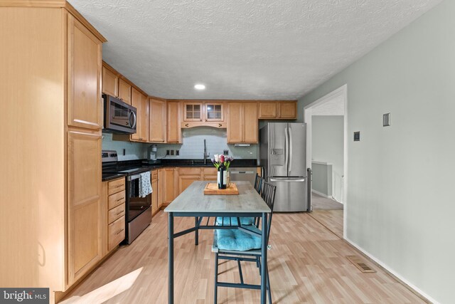 kitchen with decorative backsplash, dark countertops, light wood-type flooring, a textured ceiling, and stainless steel appliances