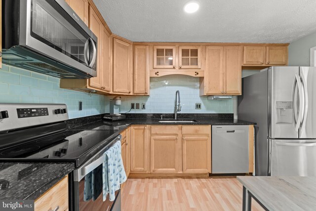 kitchen with tasteful backsplash, light wood-type flooring, a sink, dark stone countertops, and stainless steel appliances