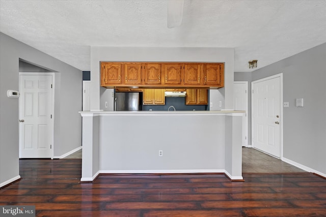 kitchen featuring baseboards, freestanding refrigerator, dark wood-style flooring, and under cabinet range hood