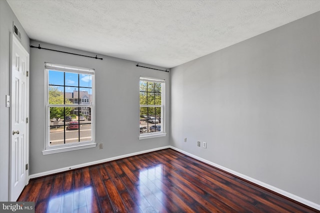 spare room featuring baseboards, a textured ceiling, wood finished floors, and visible vents