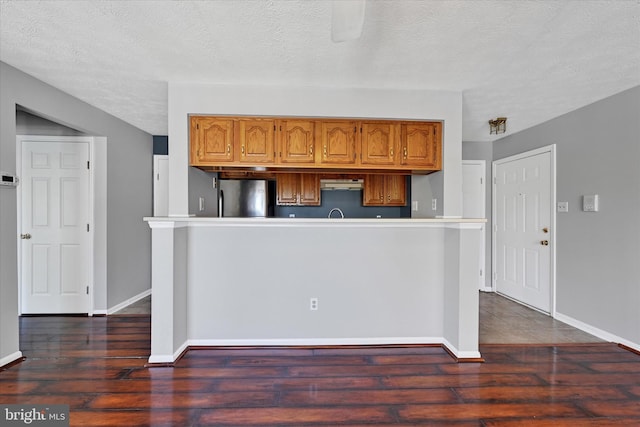 kitchen featuring freestanding refrigerator, dark wood-style flooring, a textured ceiling, and under cabinet range hood
