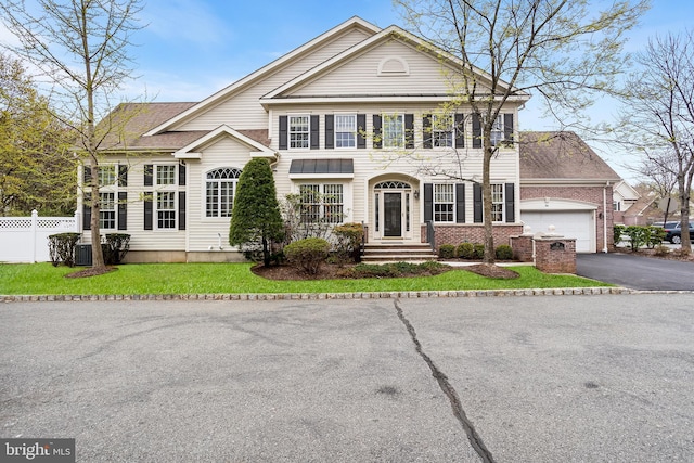 greek revival house with brick siding, fence, driveway, a front lawn, and an attached garage