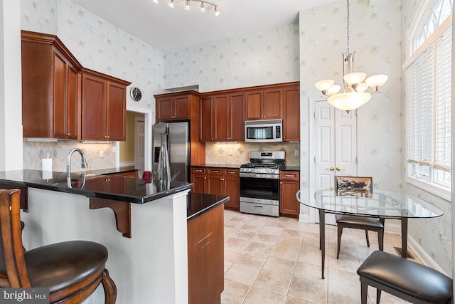 kitchen with an inviting chandelier, dark countertops, stainless steel appliances, and wallpapered walls