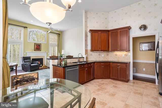 kitchen featuring a sink, appliances with stainless steel finishes, a healthy amount of sunlight, a warm lit fireplace, and wallpapered walls