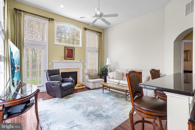 living area with visible vents, arched walkways, a glass covered fireplace, dark wood-type flooring, and a ceiling fan