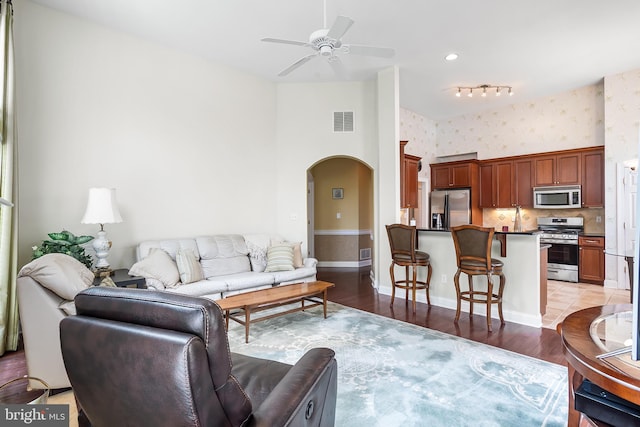 living room with visible vents, ceiling fan, wallpapered walls, arched walkways, and light wood-type flooring