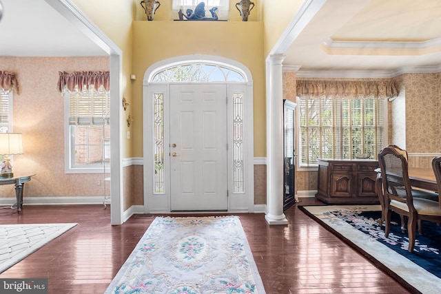 foyer entrance with a healthy amount of sunlight, wallpapered walls, ornate columns, and dark wood-style floors