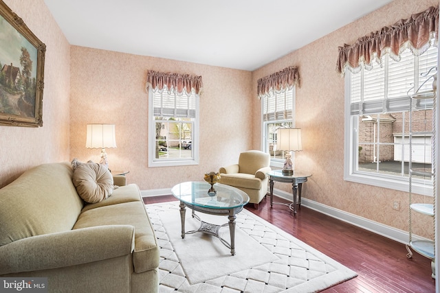 living room featuring dark wood-style floors, wallpapered walls, and baseboards