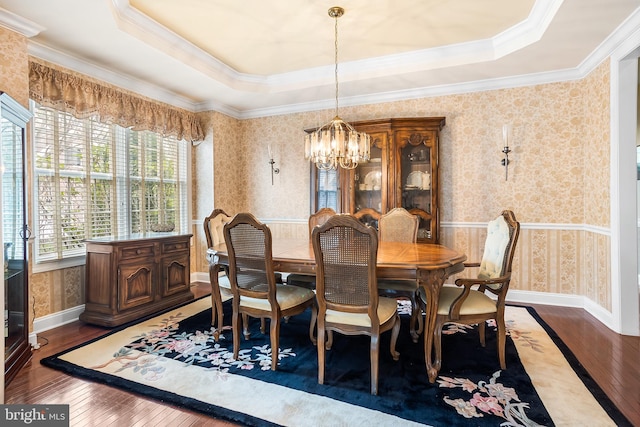 dining area featuring a chandelier, a raised ceiling, ornamental molding, wallpapered walls, and hardwood / wood-style flooring