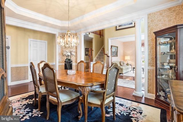 dining area featuring an inviting chandelier, ornamental molding, ornate columns, wood finished floors, and stairs