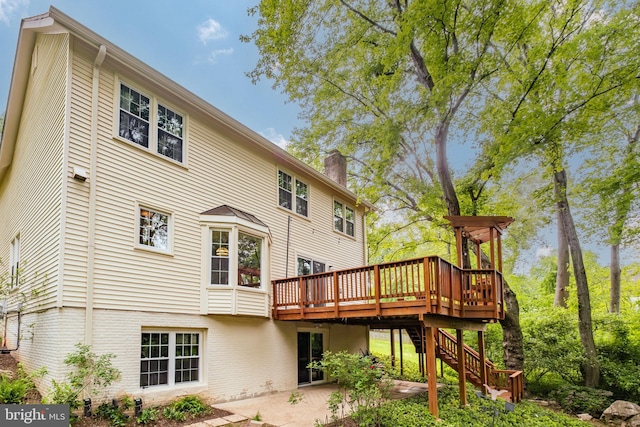 rear view of house featuring brick siding, a wooden deck, stairway, a chimney, and a patio