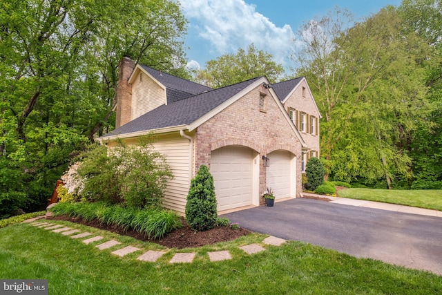 view of side of property featuring a yard, a chimney, an attached garage, and driveway