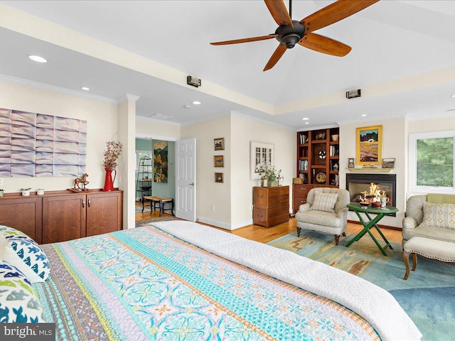 bedroom with a glass covered fireplace, ornamental molding, vaulted ceiling, wood finished floors, and baseboards