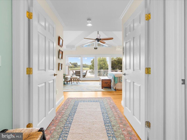 hall featuring wood finished floors, ornamental molding, and vaulted ceiling