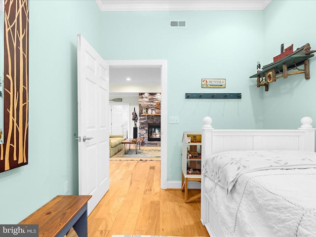 bedroom with crown molding, a fireplace, light wood-type flooring, visible vents, and baseboards